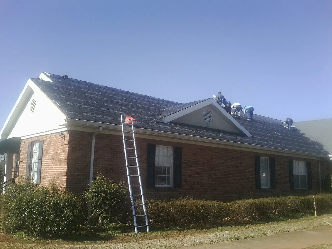 Crew tearing shingles off a brick ranch roof with a ladder set — Emergency Roof Repair work by our crew in Francitas