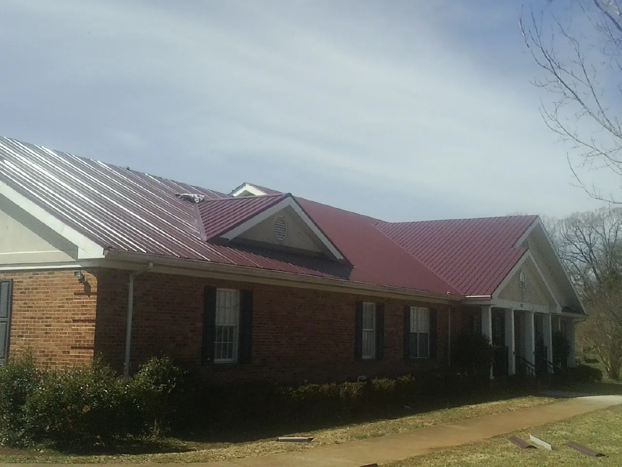 Red metal roof with gabled entries on a long brick building, from a Hail Damage Roof Repair job in Francitas