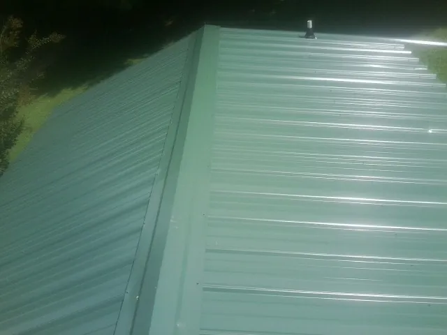 New green metal panels meeting at the ridge of a roof — Flat Roof Repair work by our crew in Francitas