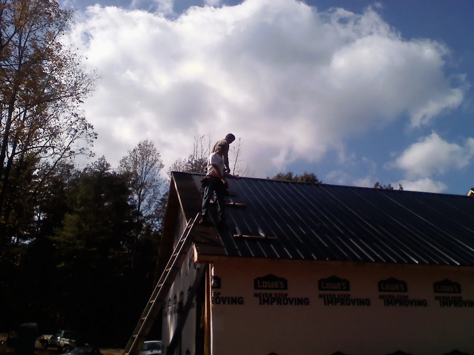 Roofer fastening dark metal panels high against a cloudy sky, from a Roof Inspection job in Francitas