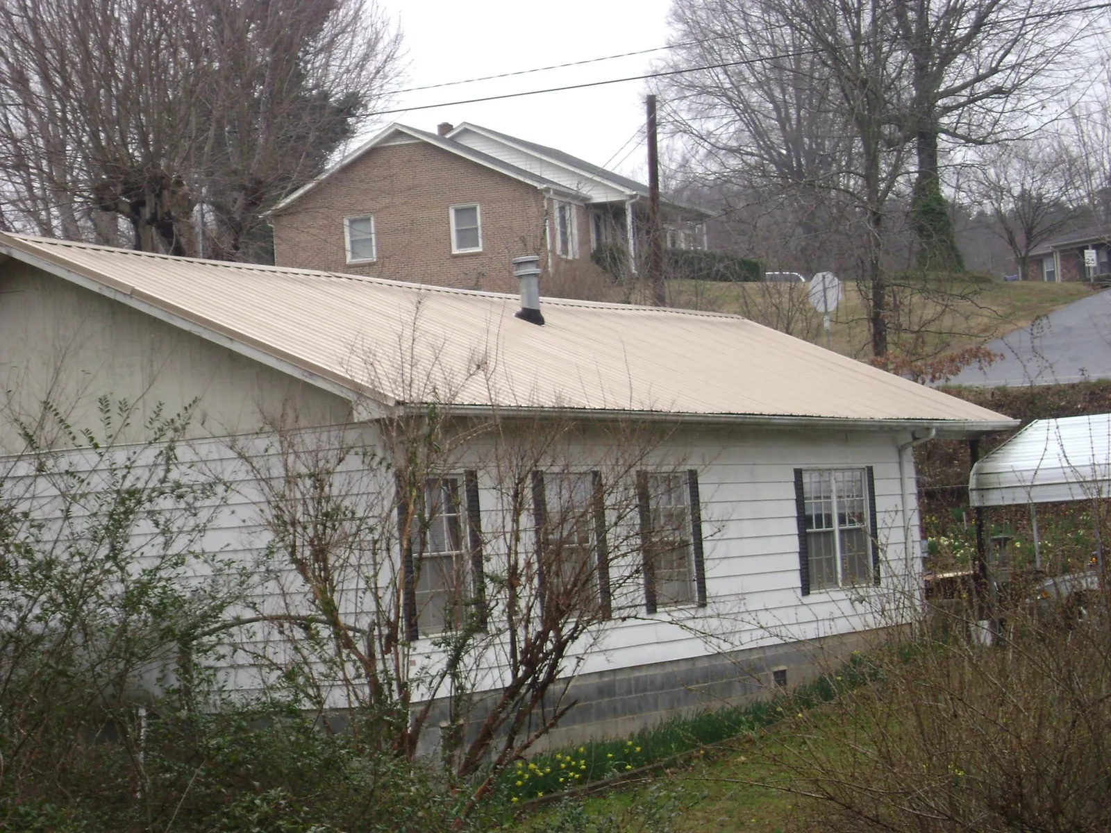 Tan metal roof on a white sided house set into a hillside — Commercial Roofing by Roofing Brothers in Francitas